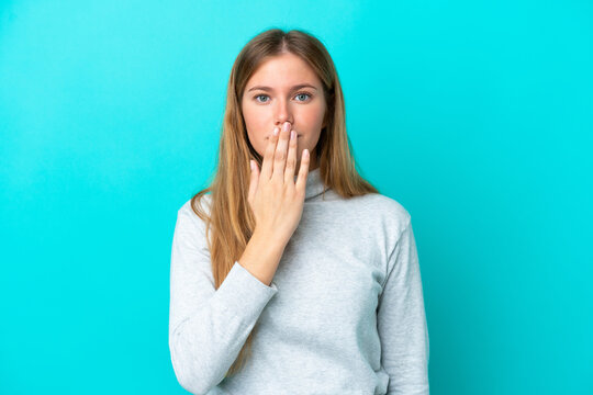 Young blonde woman isolated on blue background covering mouth with hand