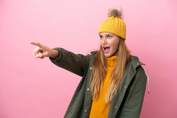 Young blonde woman wearing winter jacket isolated on pink background pointing away