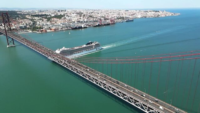 A bird's eye view of the 25 de Abril Bridge (Portuguese: Ponte 25 de Abril) across the Tagus river with a sailing cruise ship, Lisbon