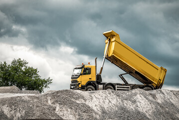 A large mining truck unloads the gravel. A soil transporter with a raised body dumps soil.