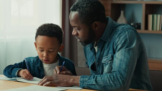African American father personal private teacher tutor teach little ethnic boy write help schoolboy with writing. Dad helping son child kid schoolchild prepare to test home lesson elementary education