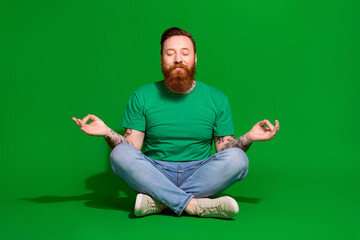 Full length photo of funky dreamy guy dressed t-shirt closed eyes practicing yoga isolated green...