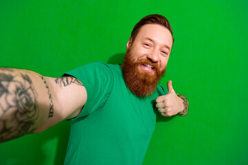 Photo of nice handsome guy with ginger beard stylish t-shirt doing selfie showing like good job isolated on green color background