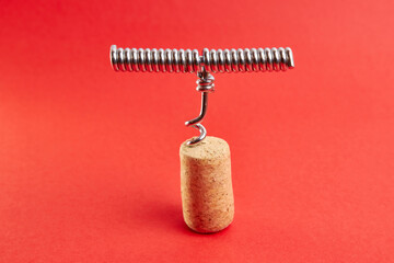 Metal corkscrew screwed into a wine cork on a red background.