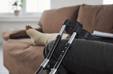 Close-up of picture of crutches against background of sitting african american woman resting at home sitting on the sofa in the living room. Rehabilitation after leg injury, severe bruise or sprain.