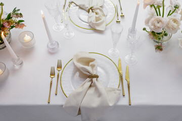 Banquet table decorated with plates, cutlery, candles, glasses and flower arrangements