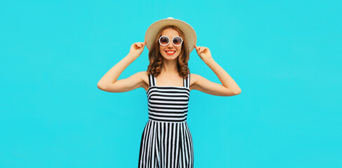 Summer portrait of beautiful young woman wearing straw round hat, striped dress on blue background
