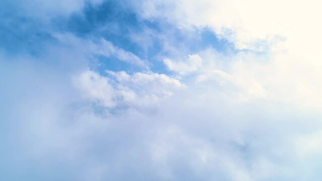 Flying through heavenly beautiful sunny cloudscape. White fluffy clouds moving softly on the sky. Clouds moving slowly on the clear blue sky in pure daylight. Cumulus white clouds. Cold atmosphere. 