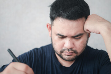 Obraz premium Asian man are tired and stressed about working on a laptop and taking notes at home. Stressful headaches from working on his desk.