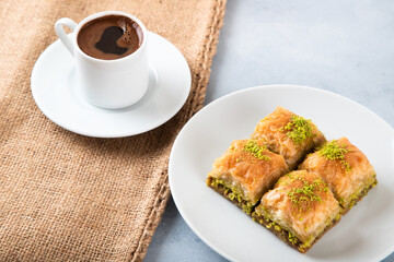 Pistachio baklava on a white plate with Turkish coffee.A plate of traditional baklava on burlap sack