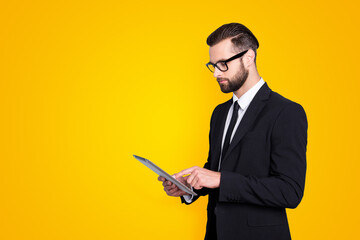 Portrait with copyspace, empty space of busy smart man with modern hairstyle, stubble, having tablet in hands, checking email, chatting with partners over grey background