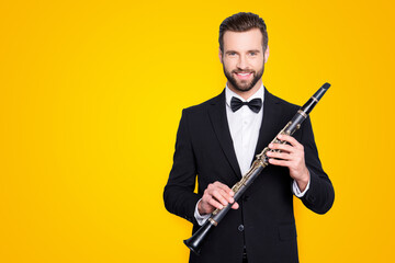 Portrait with copyspace, empty place of stylish cheerful man with hairstyle in black tux holding bassoon in hands, looking ta camera, isolated on grey background