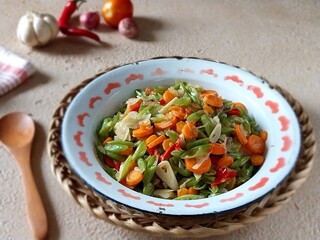 Stir fried bean and carrot or oseng buncis wortel is kind of Indonesian daily menu. Served in enamel plate on table with ingredients in background. Focus selection.