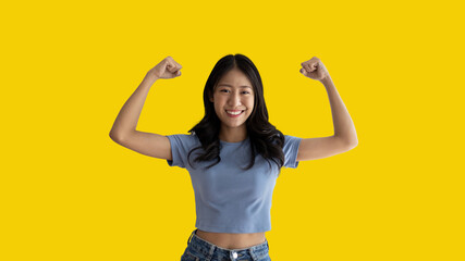 Woman flexing her muscles, Young Asian woman shows off her strength by flexing her jaw and showing off her power, Healthy, Happiness of your choice, Yellow background.