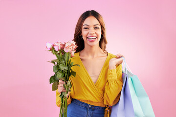 Happy, shopping bags and flowers with portrait of woman in studio for retail, birthday and spring. Event, party and smile with female and roses on pink background for sale, discount and romance