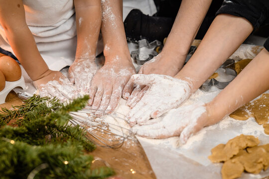Close-up shot of many unrecognizable adult and child hands kneading yeast dough at kitchen table with lots of wheat flour.