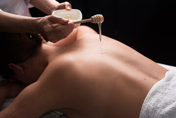 masseur doing back massage with honey in dark room