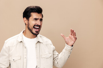 Plakat Portrait of a stylish man dissatisfied and angry screaming on a beige background in a white t-shirt looking at the camera, fashionable clothing style, copy space, space for text