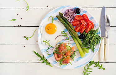 Ketogenic breakfast. Breakfast. Fried egg, crisp loaves with salmon, green asparagus, fresh tomatoes and red onions on white plate. Top view, flat lay
