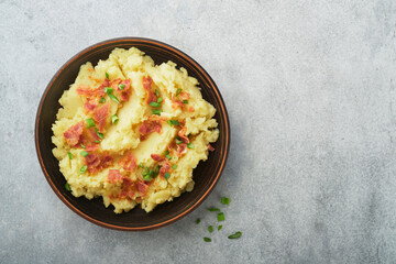 Mashed boiled potatoes. Bacon mashed potatoes with green onion, pepper and cheddar cheese in bowl on light old wooden backgrounds. Delicious creamy mashed potatoes. Top view.