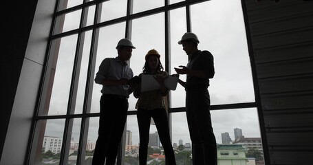 Fototapeta na wymiar Silhouette of Asian group Architect and engineer construction workers on plans with a blueprint while working for teamwork. Architects discussing business plans