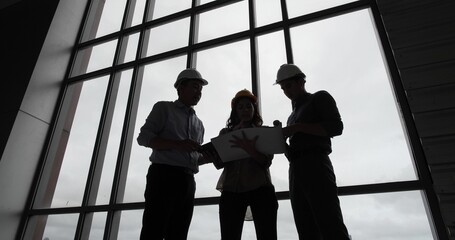 Silhouette of Asian group Architect and engineer construction workers on plans with a blueprint...