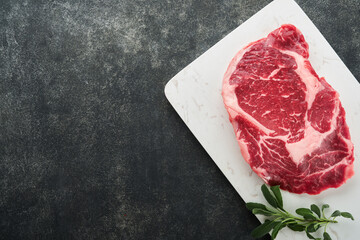Raw fresh ribeye steak or Rib-eye steak. Raw fresh marbled meat Ribeye Black Angus and seasonings pepper, rosemary, thyme and salt on old wooden rustic background. Top view and copy space.