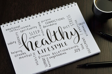 HEALTHY LIFESTYLE handwritten word cloud in notebook with cup of espresso and pens on black wooden desk