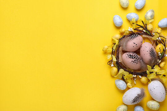 Decorative nest with many painted Easter eggs on yellow background, flat lay. Space for text