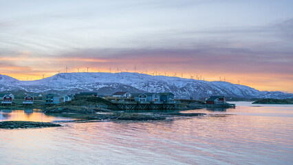 Sonnenaufgang mit Morgenrot über der Insel Kvaløya mit Windrädern und dem Dorf Sommarøy im Vordergrund. bunte Häuser am Ufer des Atlantik in Norwegen bei Tromsø