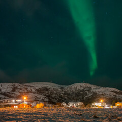 Fototapeta na wymiar wunderbare Nordlichter über dem Dorf Hillesøy. Hell erleuchtete Häuser und Straßenlaternen bilden einen starken Kontrast zum dunklen Himmel mit der grünen Aurora Borealis. Winterstimmung in Norwegen