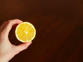 The hand holds half of a yellow lemon on a dark background.
