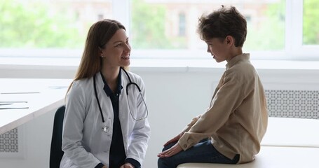 Engaged caring pretty female pediatrician with stethoscope talking to little patient boy, asking about complaints, speaking, smiling, laughing, examining child in doctor office - Powered by Adobe