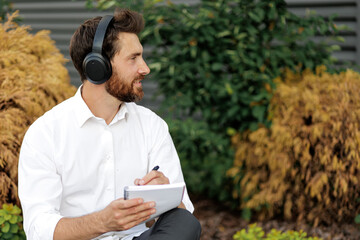 Fototapeta premium Man listening music in headphones while writing in diary