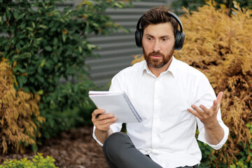 Puzzled brunette businessman with notebook gesturing, thoughtfully looking ahead outdoors.