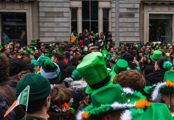 Green hat in the crowd, people in the street with costumes, irish flag colours, Paddy's day parade...