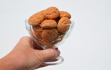 Hand holding traditional Italian almond cookies amaretti in a glass bowl on a white background.
Famous amarettini cookie biscuits.Delicious Christmas pastry popular in Italy.