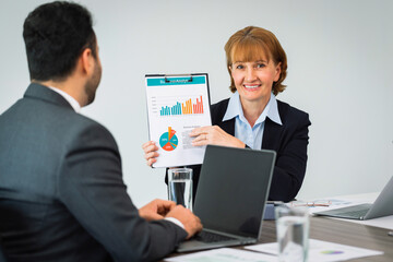 Middle aged female accountant smiling happily showing graph and looking at camera before meeting with boss