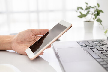 Asian businesswoman using laptop and checking smart phone, close up clean image in front of the window in soft light..
