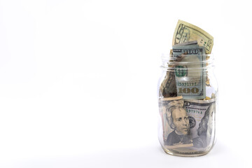 Side profile of an isolated glass mason jar stuffed full of cash or USD paper currency as a financial savings or investment concept positioned to the right side with white background and copy space.