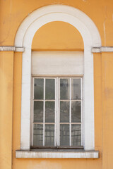 The white colored window of a yellow building, the grilles on the window.