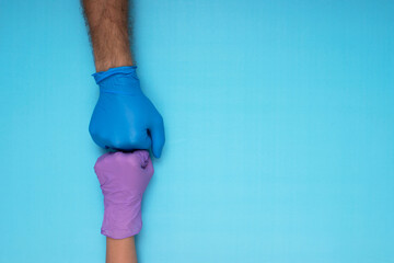 two doctors wearing medical gloves clenched fists on a light blue background