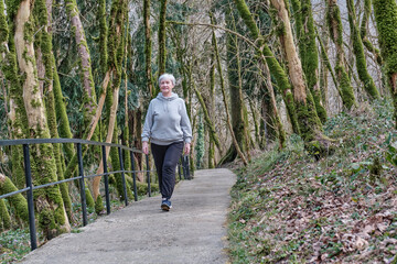 Senior woman walking along tourist trail in relic forest.