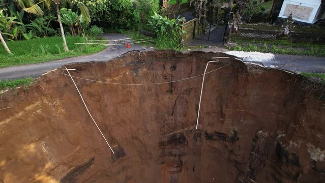 Flying up close to edge of ruined road, then reveal general view of calamity. Buildings of house compound are now at risk of further ground collapse in unstable location. Terrible local landslide