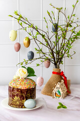 Fresh flowering branches decorated with Easter colorful eggs in a vase, Easter cake on the table. Holiday concept, home decoration, happy childhood and family traditions