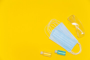 Protective glasses, face mask and alcohol sanitizing gel, antiseptic on yellow background. Coronavirus personal protective equipment.