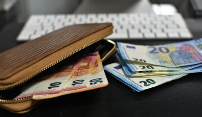 euro bills and wallet, computer and keyboard on the table