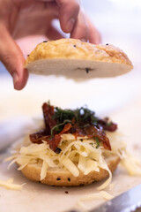 Chef preparing a bagel with cheese, bacon and basil. Hand holds bread