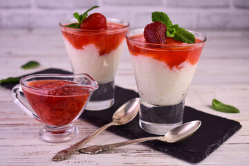 Rice pudding with strawberry jam in glasses on a white wooden background.	