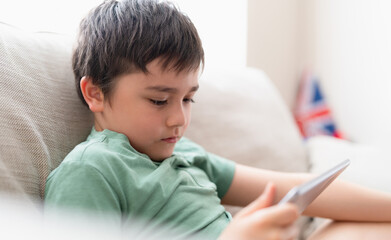 Education concept,School kid using tablet readying story from internet,Boy studying online learning at home,Child holding digital pad using wifi playing game or chatting with friends.Back to School